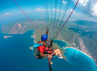 Paraglider tandem flying over the sea with blue water and mountains in bright sunny day. Aerial...