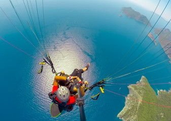 Paraglider tandem flying over the sea with blue water and mountains in bright sunny day. Aerial...