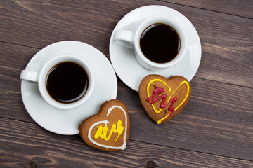 Two cups of coffee and cookies in the shape of a heart on a wooden table on Valentine's Day