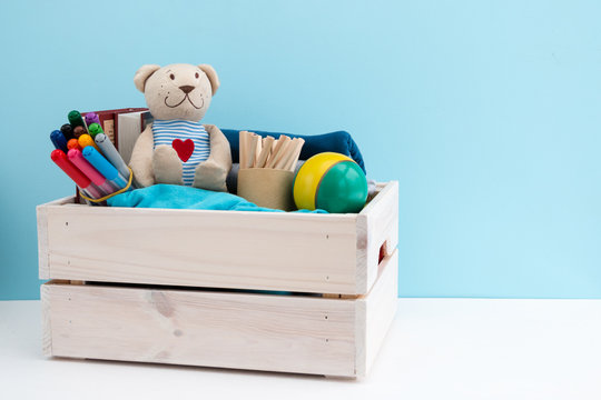 Wooden box with donations: children's toys, stationery and children's clothing. Concept: you can help, they need help. Background, free space for inscription. Red heart on the chest of a teddy bear.