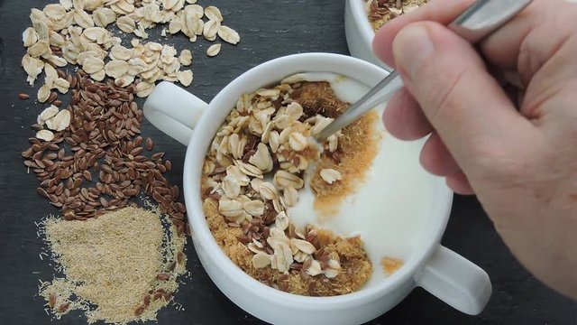 Male hand spoon mixes superfood with yogurt, bran and flax seeds. Healthy breakfast with white yogurt or kefir, bran, oatmeal and flaxseeds. Eco food. Fermented Dairy Products