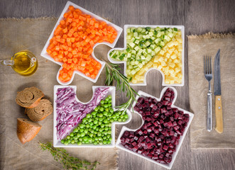 Delicious fresh pieces of vegetables of carrots, cucumber, potatoes, beets and peas close-up with fresh onion and olive oil on a bag cloth on a rustic gray table.