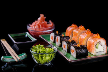 Japanese food. A set of various rolls of salmon, eel, shrimp and red caviar, in a beautiful green bowl, on a black background with reflection.