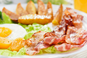 Fried bacon with French fries and a delicate egg, close-up.
