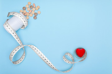 White jar of medications wrapped in a flexible ruler for fitness.Blue background with heart and copy space.Concept of losing weight when taking BIO supplements. Healthy lifestyle.