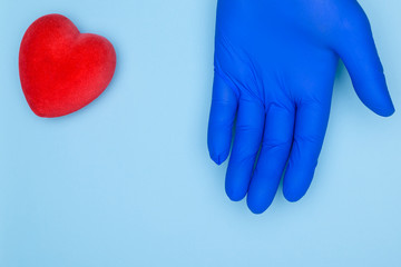 Doctor's hand in blue gloves and red heart on blue background.Cardiology and heart disease concept.Health insurance or love concept.