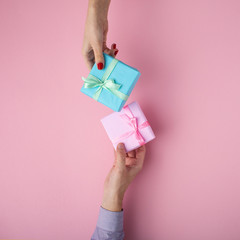 man and girl exchanging gifts from hand to hand,boxes wrapped in decorative paper with a bow on pastel background, the concept of holidays and love , top view