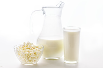Fresh milk in a glass poured from a jug with a bowl of cottage cheese on a white background. Dairy products in the morning for breakfast are very useful for children's health.