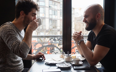 Two young guys with beards drink a coffee and having a nice conversation.