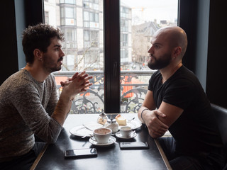 Two young guys friends with beards arguing in a coffee shop