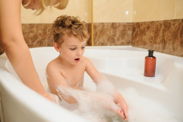 Little boy washing and playing in bathtub with foam and soap bubbles with his mother