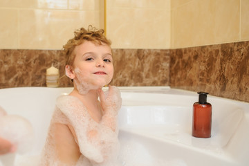 Little boy washing and playing in bathtub with foam and soap bubbles