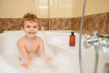 Little boy washing and playing in bathtub with foam and soap bubbles
