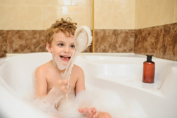 Little boy washing and playing in bathtub with foam and soap bubbles