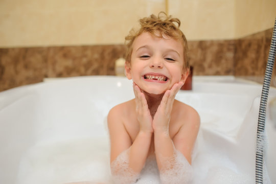 Little boy washing and playing in bathtub with foam and soap bubbles