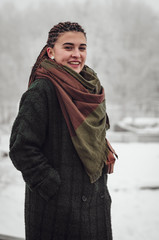 stylish photograph of a portrait of an attractive woman with long pigtails, dressed in an eco-coat and scarf, walked in a winter-frozen city