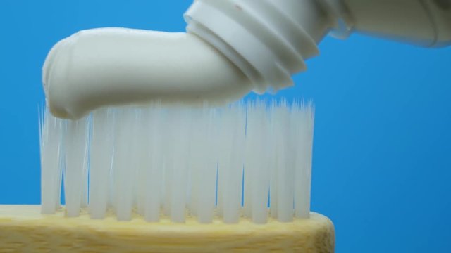 White toothpaste coming out of a tube on wooden bamboo brush at blue background