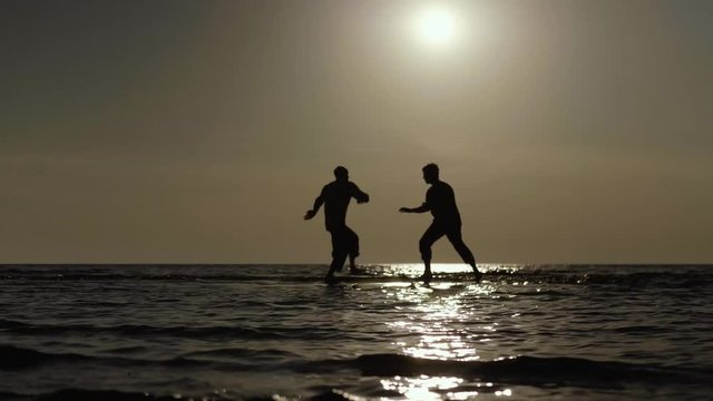 Martial artists friendly sparring on the beach at sunset in slow motion, 50 fps.