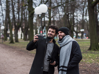 Two young guys with beard friends take a selfie, young gay couple take a selfie in a park.