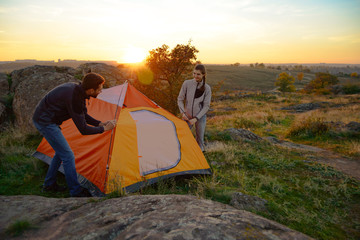 Fototapeta premium Young Couple Assembling the Tent at Sunset in the Mountains. Adventure and Family Travel.