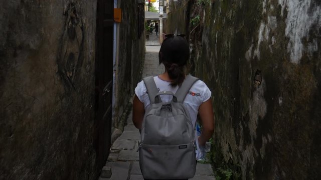 Following a girl with a backpack trough a narrow alley in Vietnam