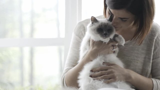 Woman holding and petting her cute cat next to a window