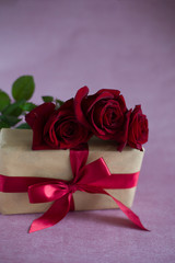 three red roses, box tied with red ribbon on pink background (vertically, close up)