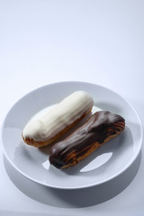 French dessert Eclair with white and black chocolate on white plate. Closeup. Selective focus. High key.