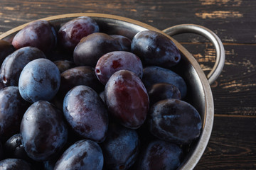 Closeup of fresh juicy plums in a metal bowl on wooden rustic background. Vegan diet. Selective focus.