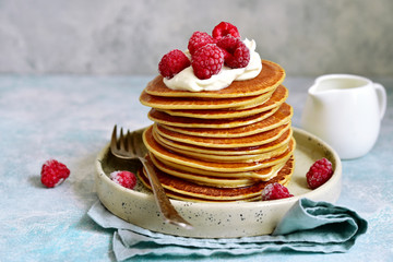 Stack of homemade delicious hot pancakes with honey, cream and raspberry.