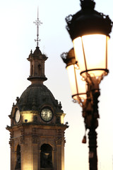 Fototapeta na wymiar Romanesque bell tower of a church with clock, bells and classic lampposts just before dawn