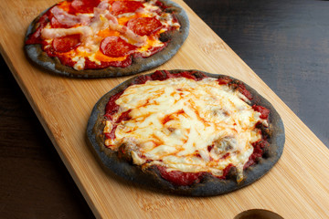 Creative pizza on black dough, two pieces on the board.