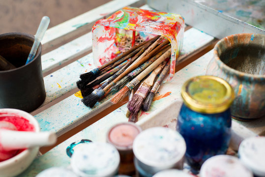 Paint brushes on technique ebru lie on a white wooden table near the cans of paint