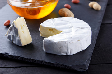 Camembert and honey on black slate board. Soft cheese with mold and peanuts on black background. Cheese and nuts on stone board