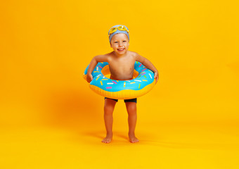 happy child boy in swimsuit with swimming ring donut on colored yellow background. © JenkoAtaman