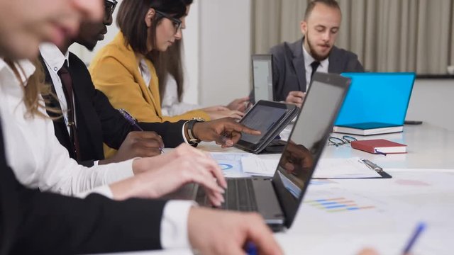 Close-up of multi-ethnic group of young business people sitting at the table on conference and working on computer tablets in the meeting room. A group of mixed business partners using technology for