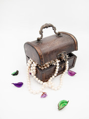 Wooden treasury chest jewelry box, slightly opened, with sea pearls showing from the inside, decorated with a few dry flower petals, isolated on a white background