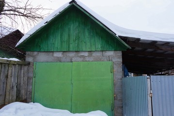 garage facade with green iron gates in the street in snowdrifts of white snow