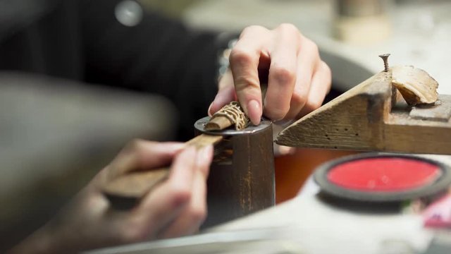 Close scene of working process.  The master is making detail for jewelry with special equipment. There are many other supplies on the background which are lying on the table.