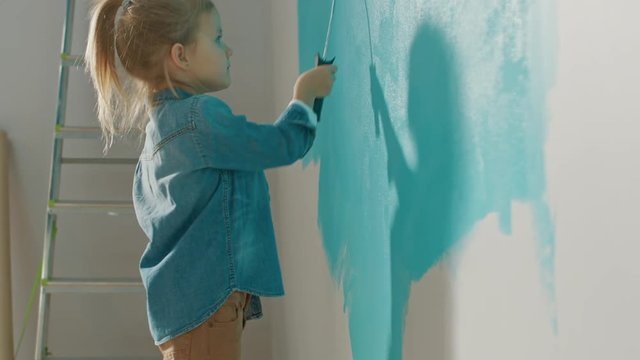 Cute Small Girl in Jeans Coat is Painting a Wall. She Paints with Roller that is Covered in Light Blue Paint. Room Renovations at Home.