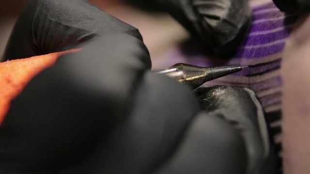 Tattoo artist fills tattoo and draw the line on skin of his client, macro view.