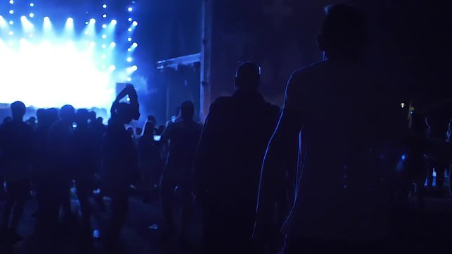 a guy drinking from a plastic cup at the concert, while people are dancing in slow motion