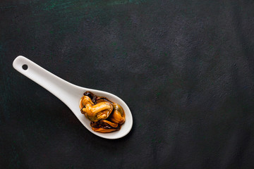 CUCHARA BLANCA DE PORCELANA CON MEJILLONES SOBRE FONDO OSCURO