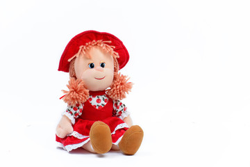 Soft doll in a red dress and hat on a white background. Children's toy. Close-up.