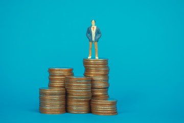 Figure miniature businessman or small people investor and office worker secretary standing on coin stack, for money and financial business success concept.