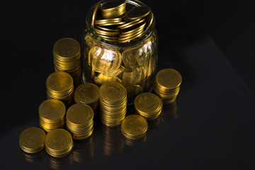 Coins stacks and gold coin money in the glass jar on dark background, for saving for the future banking finance concept.