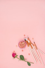  Cosmetics, makeup brushes and flowers on a pink background. Close-up. Top view.
