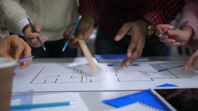 Close-up of diverse hands blueprinting plan of new building with triangle, ruler and pencils while working together on drawing. Multi ethnic architect team sketching a construction project in office.