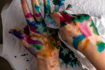 A child cleans up hands that are covered in red, pink, yellow, orange, red, blue, green, and purple ink.  Concepts: art, education, play, watercolor, finger painting, mess, creativity, fun, enjoyment,