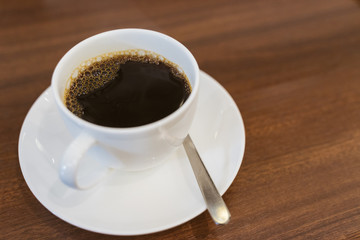 Close up hot espresso with bubbles in white coffee cup on wood table near window in coffee shop in the morning in vintage soft tone, black caffeine to stay awake for people